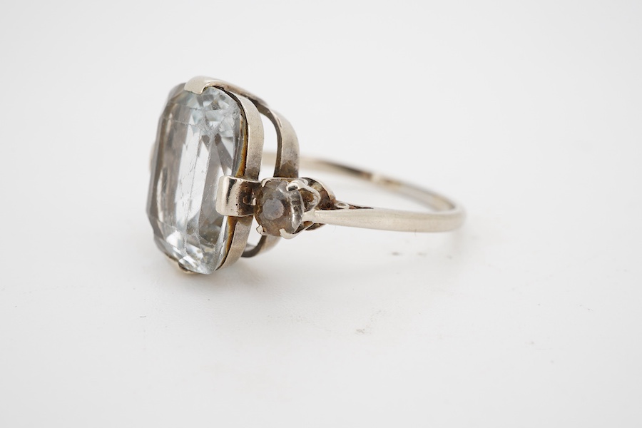 A mid 20th century white metal and single stone cushion cut blue topaz set dress ring, with two stone topaz set shoulders, size R.